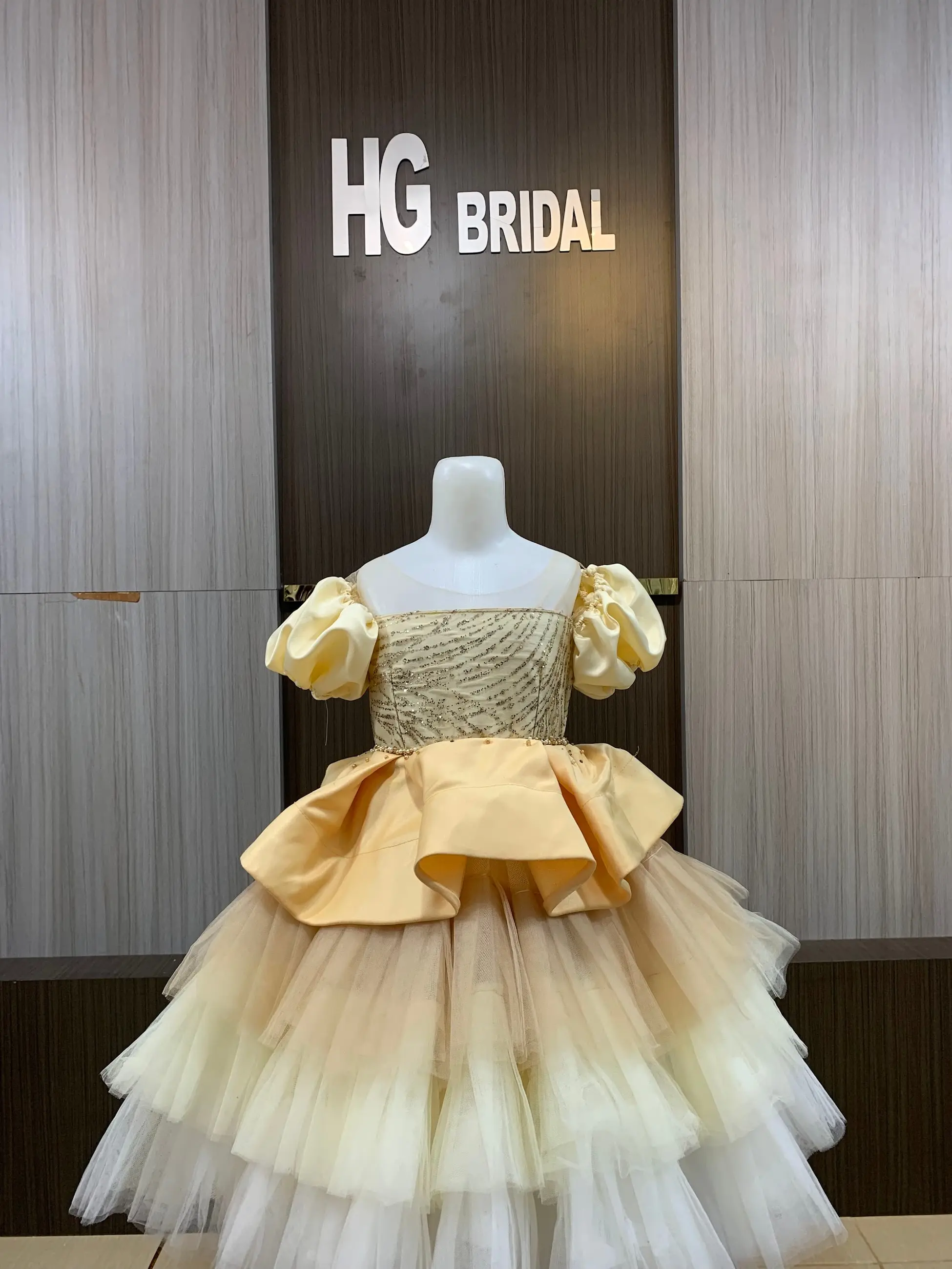 Gaun anak emas bertumpuk di manekin butik HG Bridal