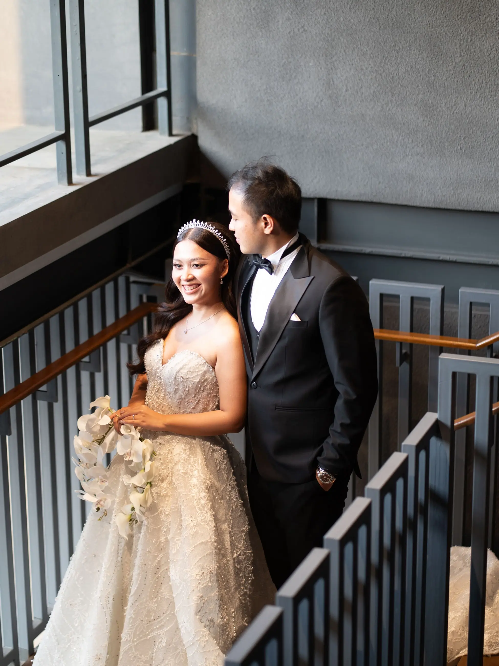 Pengantin HG Bridal dengan gaun ballgown berpayet berdiri di tangga bersama pasangannya