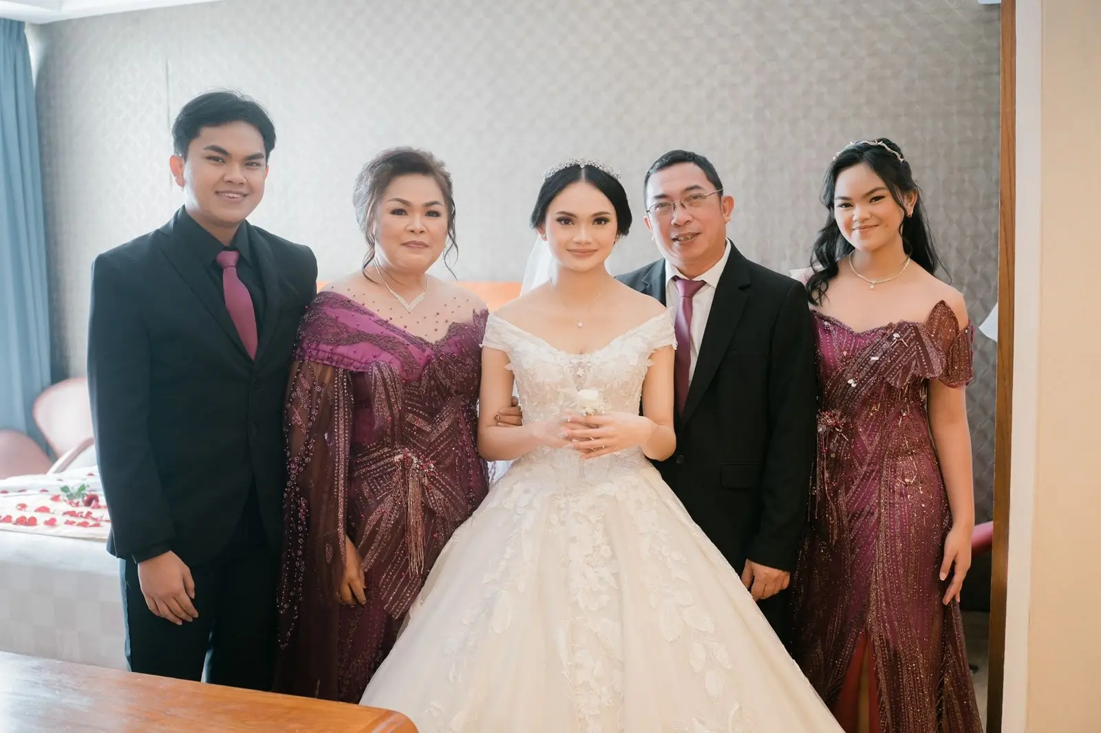 Pengantin bersama orang tua dan saudari yang memakai gaun pesta burgundy