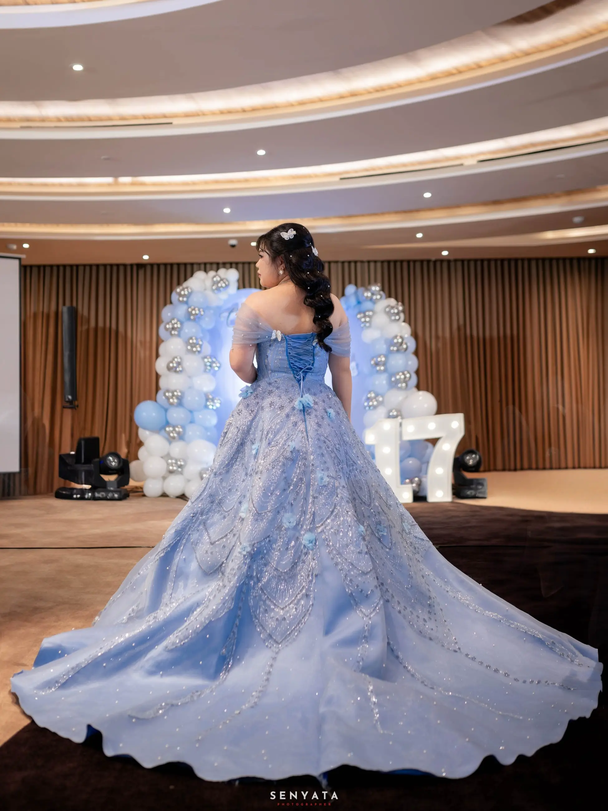 Tampak belakang ballgown biru berekor di depan dekorasi balon