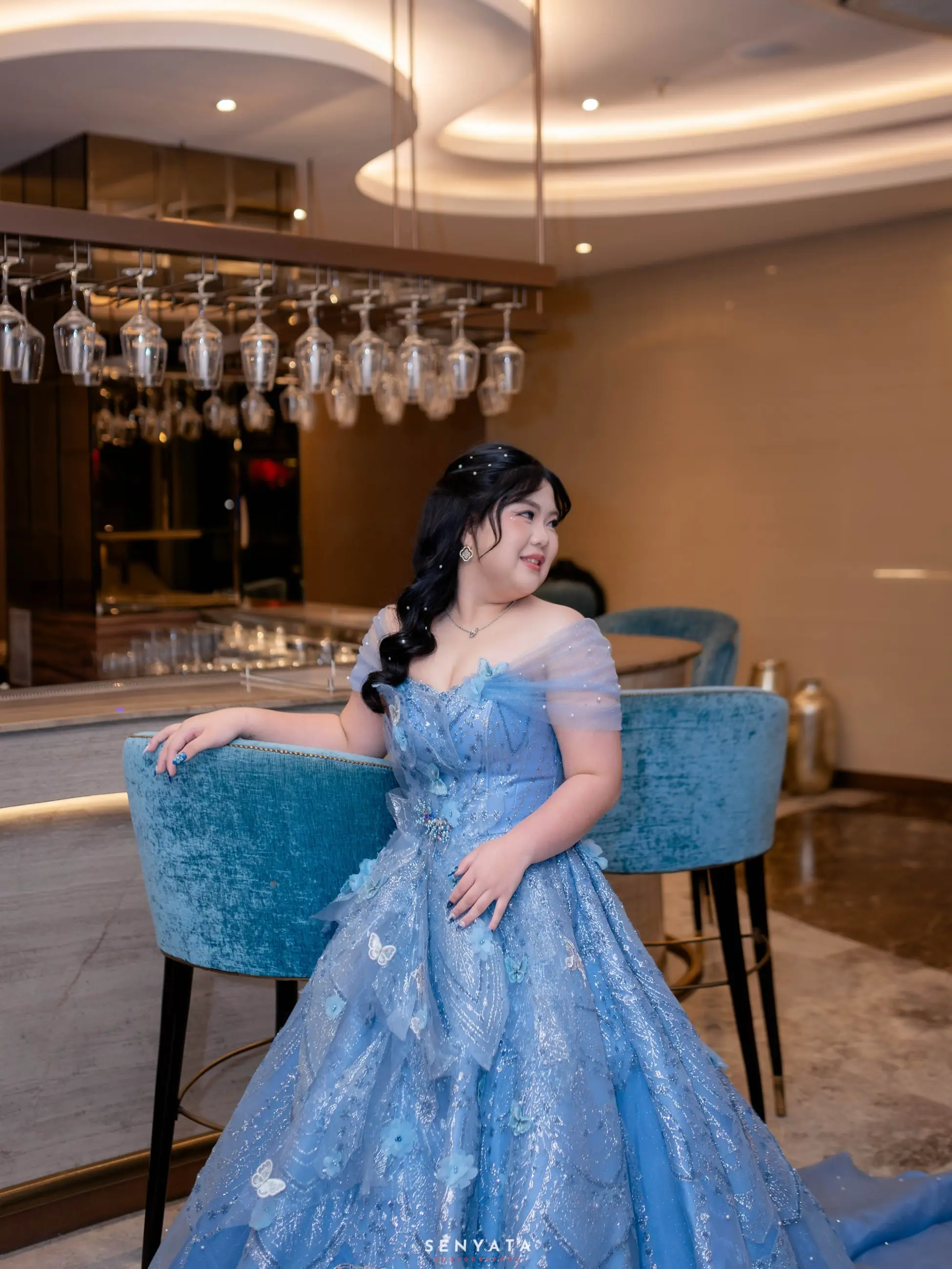 Gadis dengan ballgown biru berpayet duduk di kursi bar beludru